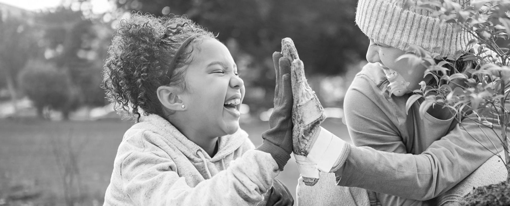 Young girl and woman high five while planting a small tree